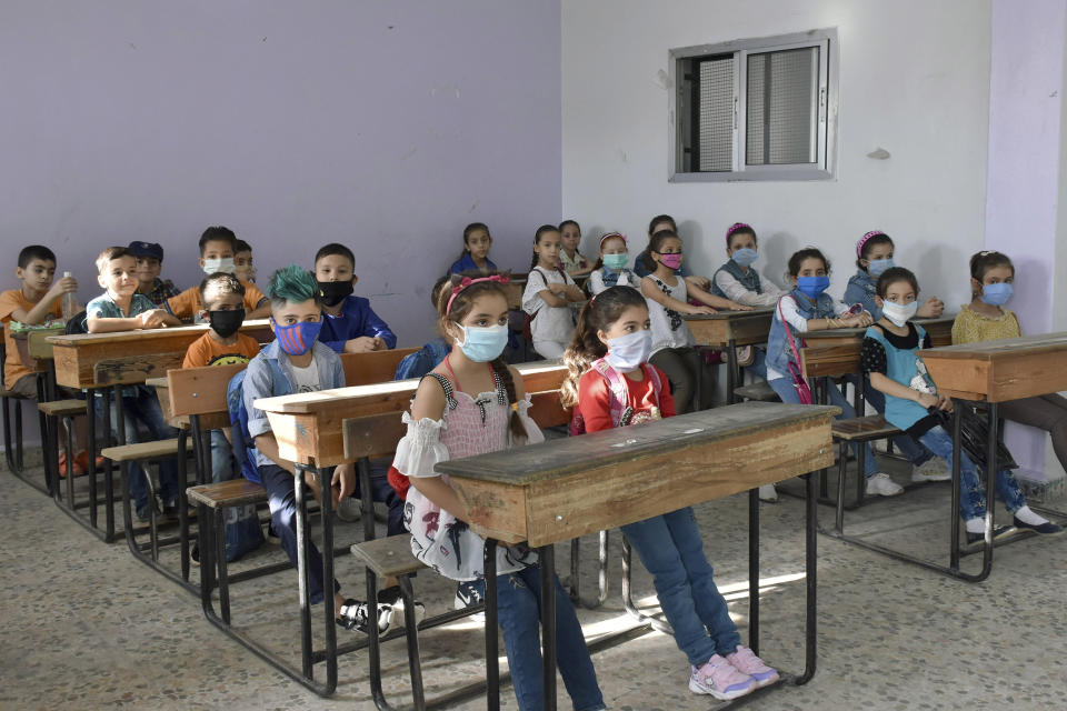 In this photo released by the Syrian official news agency SANA, students wear masks during a lesson on their first day back at school, in Hama province, Syria, Sunday, Sept. 13, 2020. More than 3 million students went to school in government-held areas around Syria Sunday marking the first school day amid strict measures to prevent the spread of coronavirus. (SANA via AP)