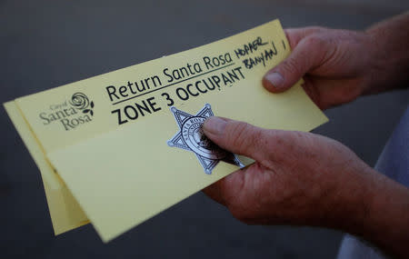 A man holds a pass from the Santa Rosa police department that allows him to come and go from the evacuation zone he lives in after a wildfire tore through adjacent streets in Santa Rosa, California, U.S., U.S., October 15, 2017. REUTERS/Jim Urquhart