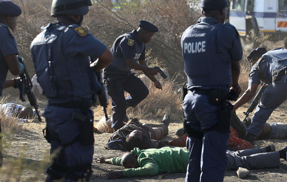 RETRANSMISSION FOR ALTERNATIVE CROP Police surround the bodies of striking miners after opening fire on a crowd at the Lonmin Platinum Mine near Rustenburg, South Africa, Thursday, Aug. 16, 2012. South African police opened fire Thursday on a crowd of striking workers at a platinum mine, leaving an unknown number of people injured and possibly dead. Motionless bodies lay on the ground in pools of blood. (AP Photo)