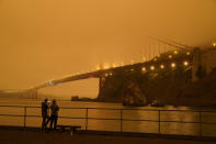 Patrick Kenefick, left, and Dana Williams, both of Mill Valley, Calif., record the darkened Golden Gate Bridge covered with smoke from wildfires Wednesday, Sept. 9, 2020, from a pier at Fort Baker near Sausalito, Calif. The photo was taken at 9:47 a.m. in the morning. (AP Photo/Eric Risberg)