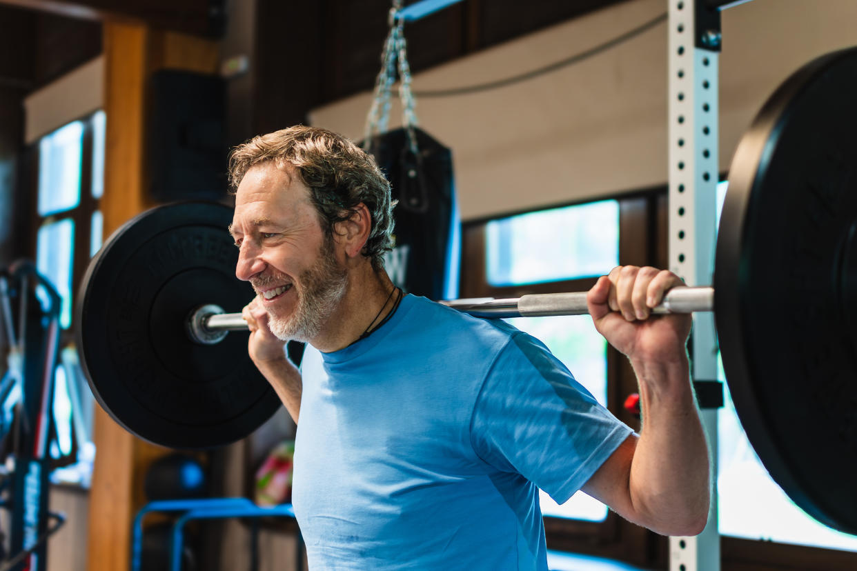 A man is lifting a heavy weight bar with a smile on his face. He is wearing a blue shirt and he is enjoying himself