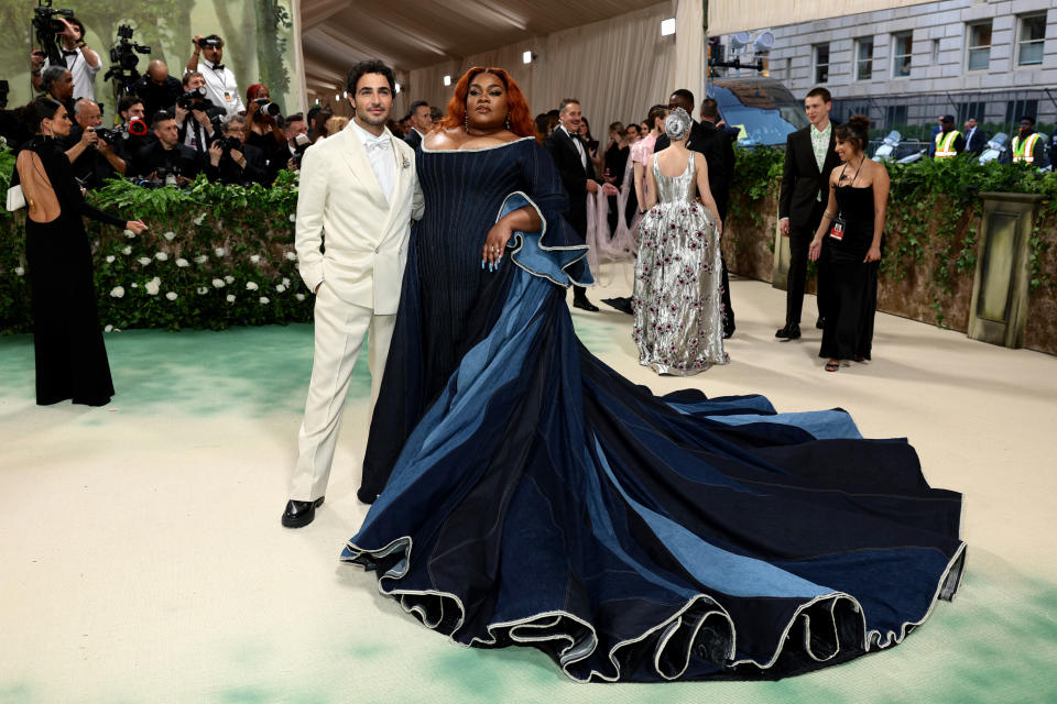 Zac Posen and Da'Vine Joy Randolph on red carpet. Posen wears a white tuxedo, and Lee in a flowing navy dress with a dramatic train at a formal event