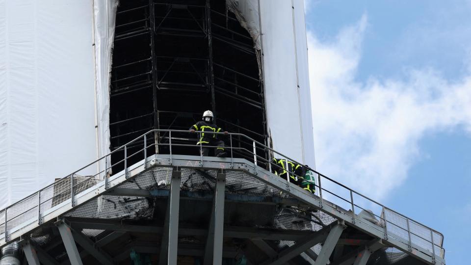 A close up photo of the plastic sheeting that was damaged by the fire. Two firefighters can be seen on the ledge surrounding the spire.
