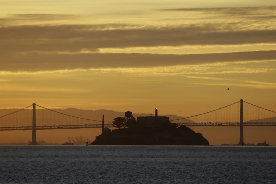 In this photo taken Feb. 1, 2018, Alcatraz Island is seen at sunrise on San Francisco Bay in this view from Sausalito, Calif. In the background is the San Francisco-Oakland Bay Bridge. The week of Nov. 18, 2019, marks 50 years since the beginning of a months-long Native American occupation at Alcatraz Island in the San Francisco Bay. The demonstration by dozens of tribal members had lasting effects for tribes, raising awareness of life on and off reservations, galvanizing activists and spurring a shift in federal policy toward self-determination. (AP Photo/Eric Risberg)