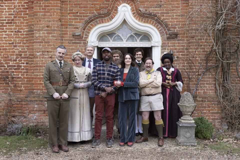 in a scene from ghosts series 5, a group of people dressed in clothes from different time periods stand outside the doorway of a stately home