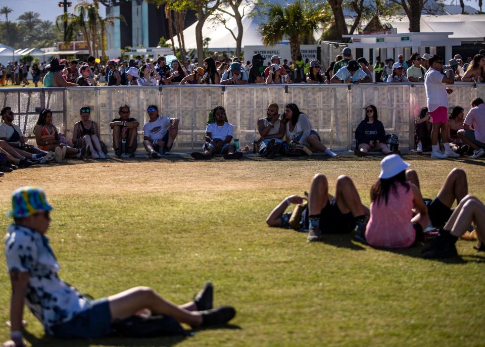 Festivalgoers look for shade along a barrier near the Outdoor Theatre during the Coachella Valley Music and Arts Festival at the Empire Polo Club in Indio, Calif., Friday, April 21, 2023. 