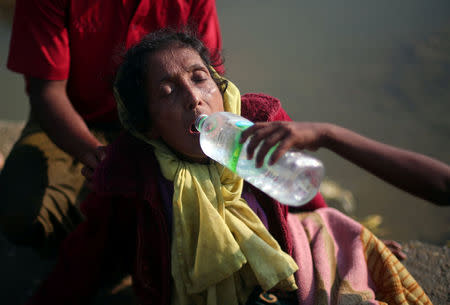 Nurij, 65, an exhausted Rohingya receives water after she is carried to a port after crossing from Myanmar, in Teknaf, Bangladesh, October 25, 2017. REUTERS/Hannah McKay