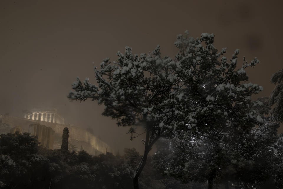 Snow covers a tree in central Athens with the ancient Parthenon temple on the Acropolis hill seen in the background, early Tuesday, Feb. 16, 2021. A cold weather front has hit Greece, sending temperatures plunging from the low 20s degrees Celsius (around 70 Fahrenheit) on Friday to well below freezing on Monday, and seeing snowfall in central Athens. (AP Photo/Petros Giannakouris)