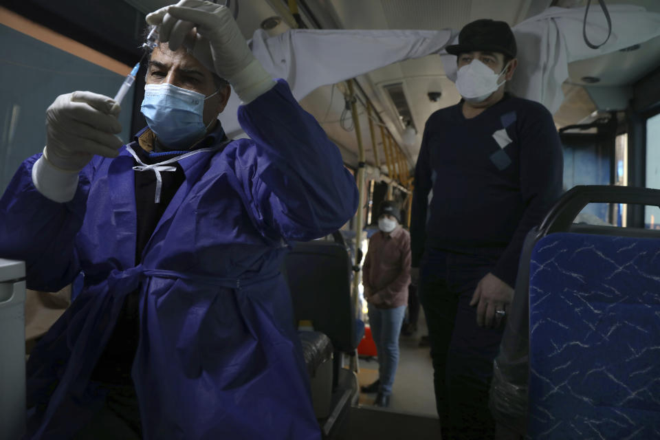 A health worker prepares a COVID-19 vaccine at a mobile vaccine clinic bus at the Grand Bazaar of Tehran, Iran, Saturday, Jan. 22, 2022. After successive virus waves pummeled the country for nearly two years, belated mass vaccination under a new, hard-line president has, for a brief moment, left the stricken nation with a feeling of apparent safety. (AP Photo/Vahid Salemi)