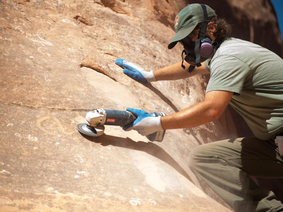 Park maintenance staff uses grinders to remove graffiti from a rock face at Arches National Park.