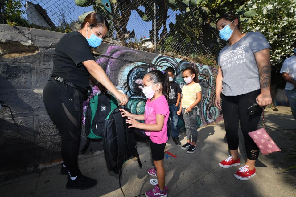 A volunteer (L) hands three-year-old Zayla a backpack filled with school supplies at distribution to support neighborhood families as her mom Claudia Rodriguez (R) looks on, August 14, 2020 in Los Angeles, California.(Photo by Robyn Beck / AFP) 