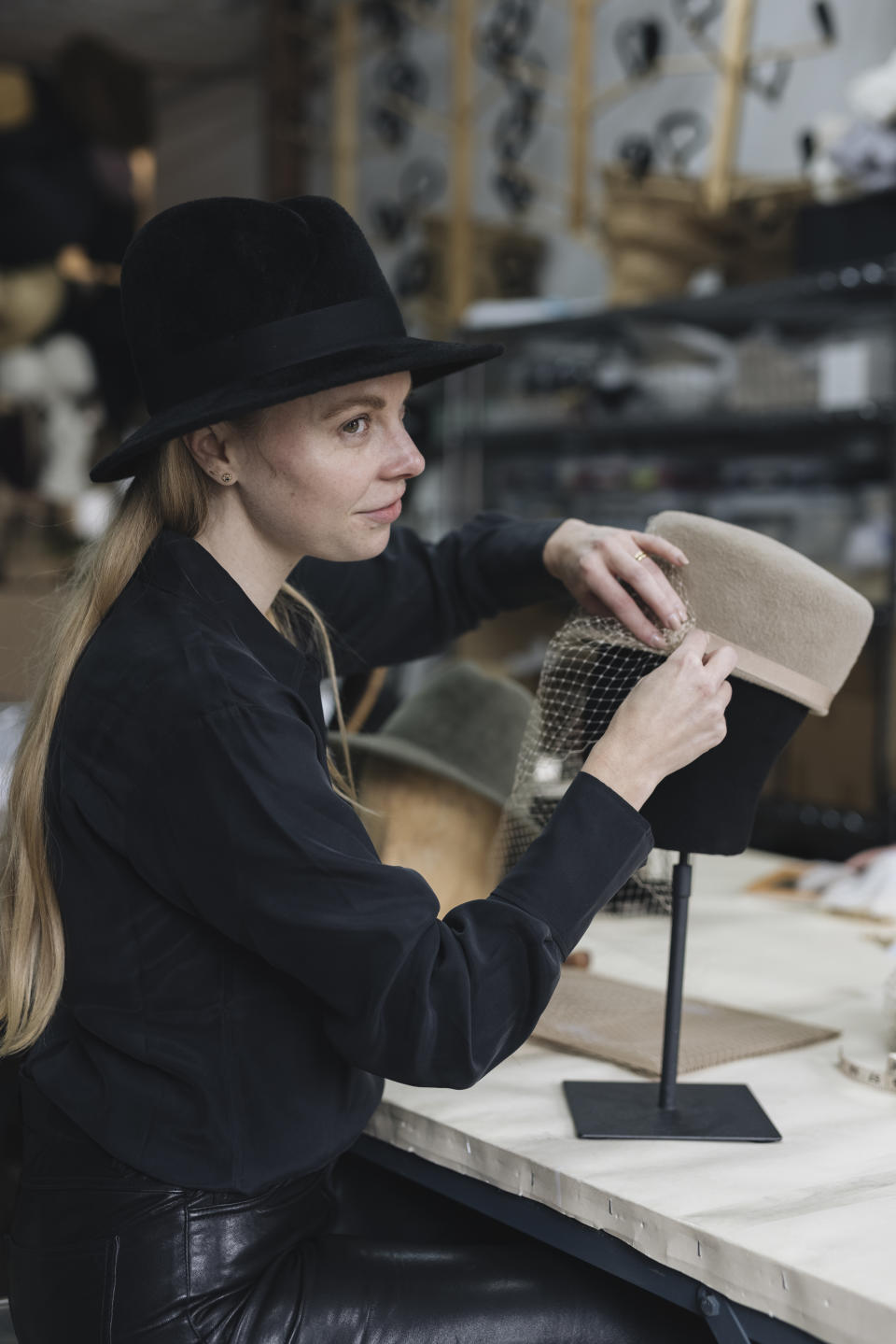 A portrait of hatmaker Gigi Burris putting a veil on one of her hats