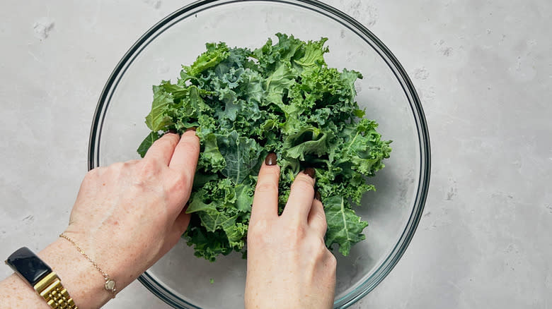 hands massaging kale in glass bowl