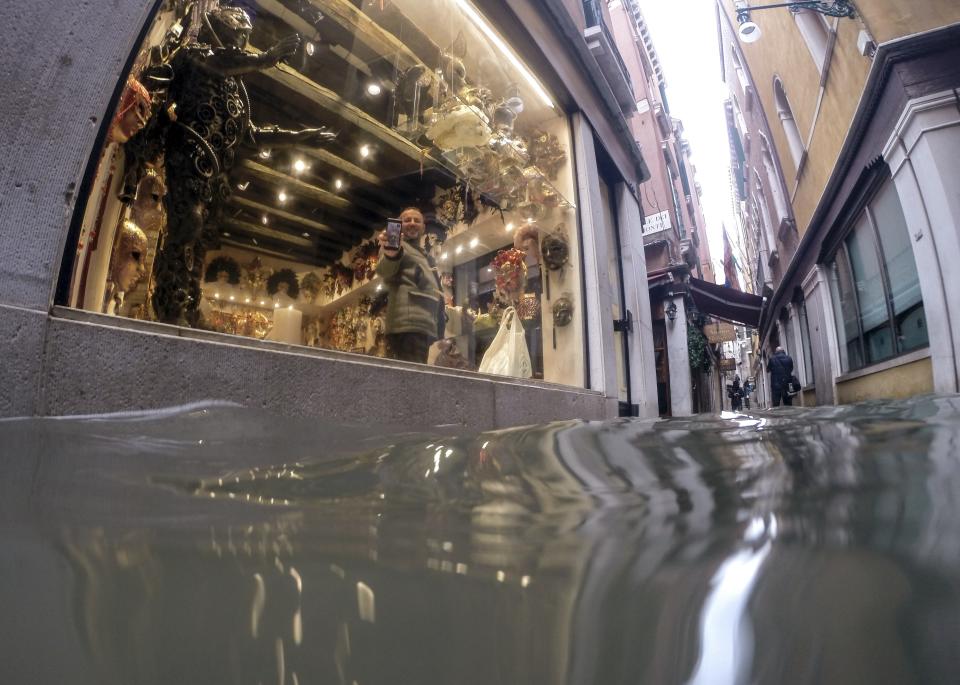 A man holds up a phone during a video call to show a a flooded alley outside a shop, in Venice, Italy, Friday, Nov. 15, 2019. Exceptionally high tidal waters returned to Venice on Friday, prompting the mayor to close the iconic St. Mark's Square and call for donations to repair the Italian lagoon city just three days after it experienced its worst flooding in 50 years. (AP Photo/Luca Bruno)