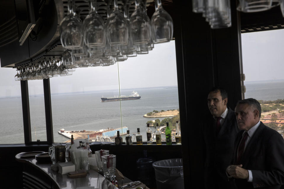 Waiters stand behind the bar at the El Girasol restaurant overlooking overlooks Maracaibo Lake where an oil taker navigates, in Maracaibo, Venezuela, May 22, 2019. El Girasol used to be a revolving restaurant, and hardly has any customers. (AP Photo/Rodrigo Abd)