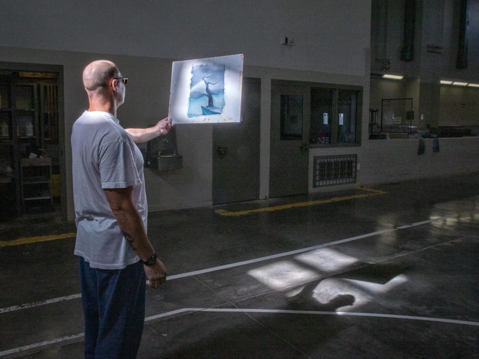 Peter Merts photos show California Prison Arts Programs A student stops to inspect his painting in window light, at Pleasant Valley State Prison - 2019