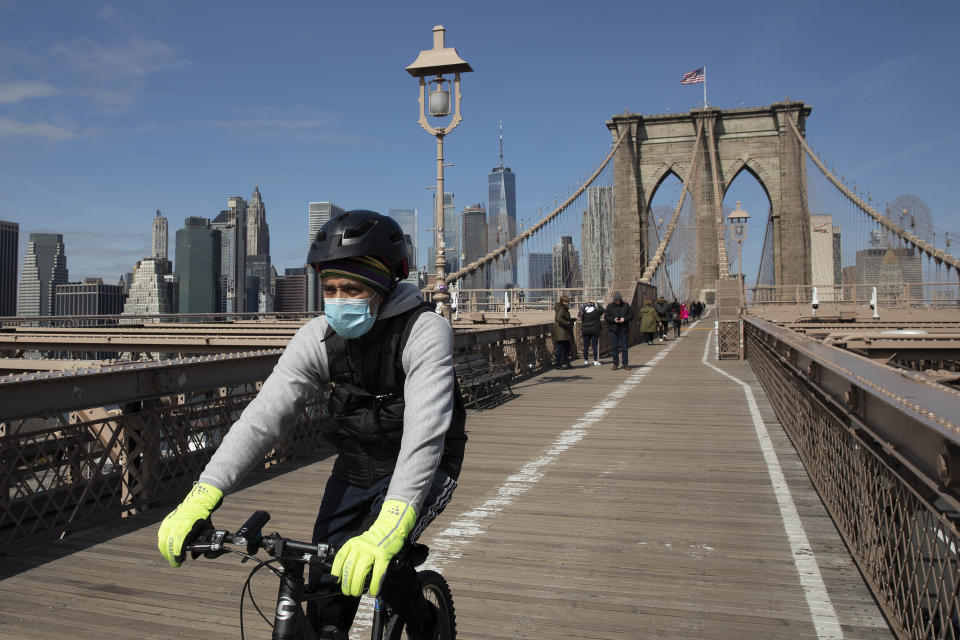 A cyclist wears a mask as he crosses the Brooklyn Bridge, Monday, March 16, 2020 in New York. The bridge's pedestrian and bicycle path is normally crowded on a sunny day. (AP Photo/Mark Lennihan)