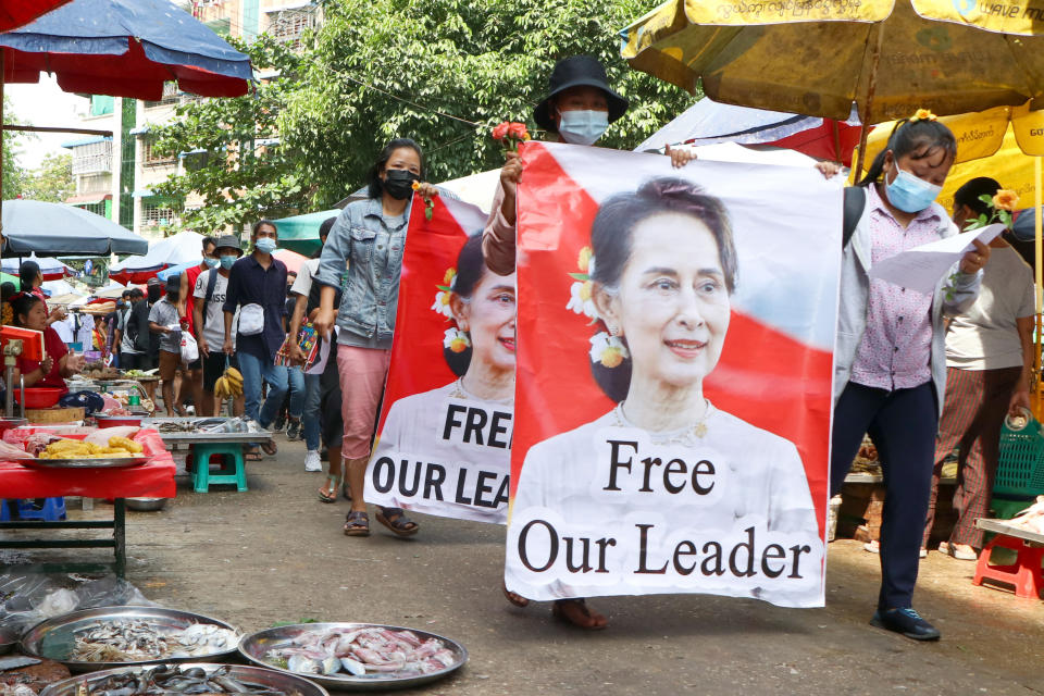 FILE - Protesters walk through a market with posters of ousted Myanmar leader Aung San Suu Kyi at Kamayut township in Yangon, Myanmar, on April 8, 2021. Myanmar’s ousted leader Aung San Suu Kyi has testified in a prison courtroom in the capital Naypyitaw for the first time in her official secrets case. Suu Kyi, who has been detained since her government was ousted last year by the military, is being tried with Australian economist Sean Turnell and three former Cabinet members on the same charge, which is punishable by up to 14 years in prison. (AP Photo, File)