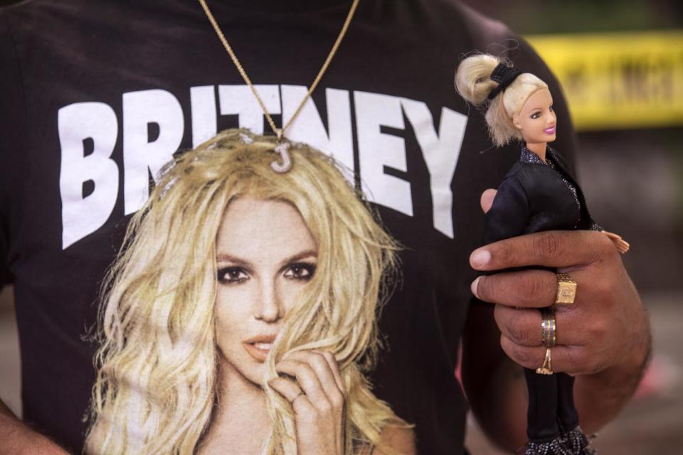 A close-up of the 'Britney' message and picture on a black shirt worn by a man holding a Britney Spears doll