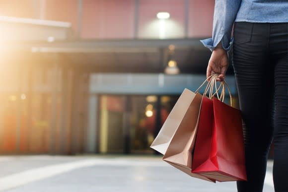 Shopper holding bags, walking toward mall entrance.