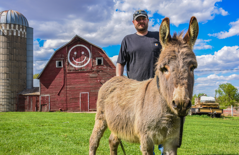 Nate Hansen and Earl the donkey pose for a photo in front of the "Smiley Barn."