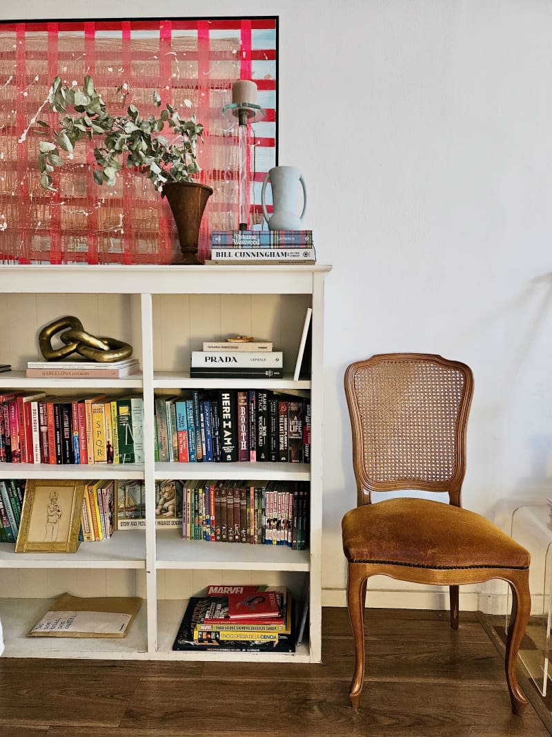 Books on a white bookshelf next to a wooden chair.