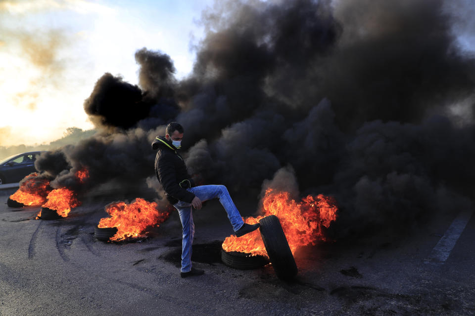 A protester kicks a burning tire to block a highway that links to the Beirut's international airport, during a protest against against the economic and financial crisis, in Beirut, Lebanon, Tuesday, March 2, 2021. The Lebanese pound has hit a record low against the dollar on the black market as the country's political crisis deepens and foreign currency reserves dwindle further. (AP Photo/Hussein Malla)