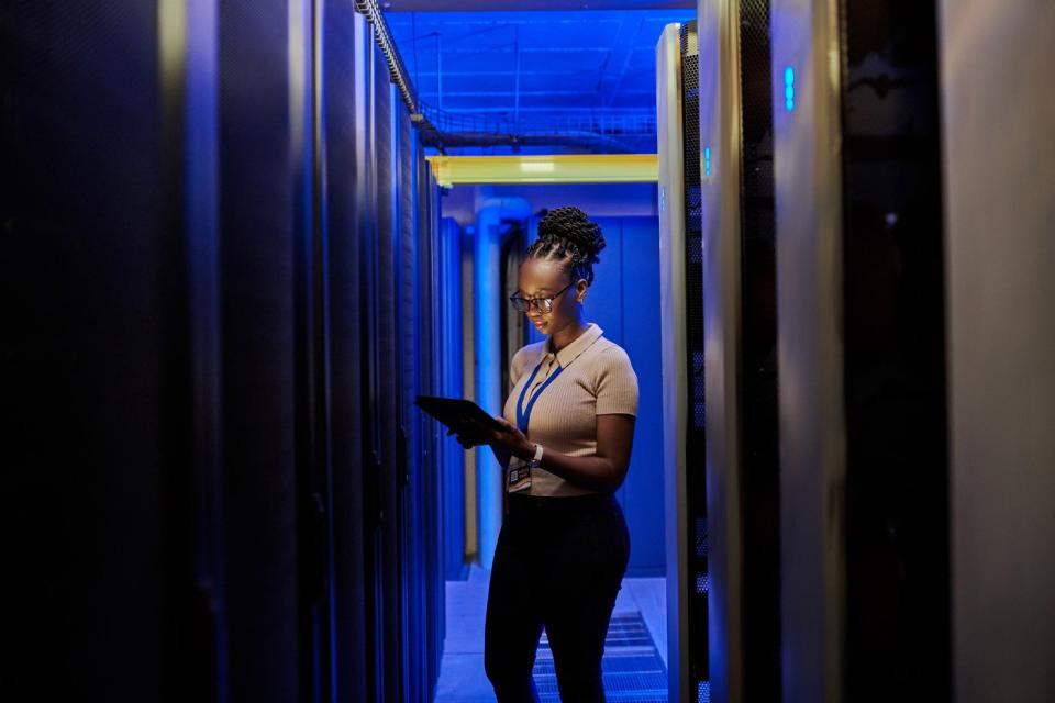 An engineer looks at a tablet while working in a server room.