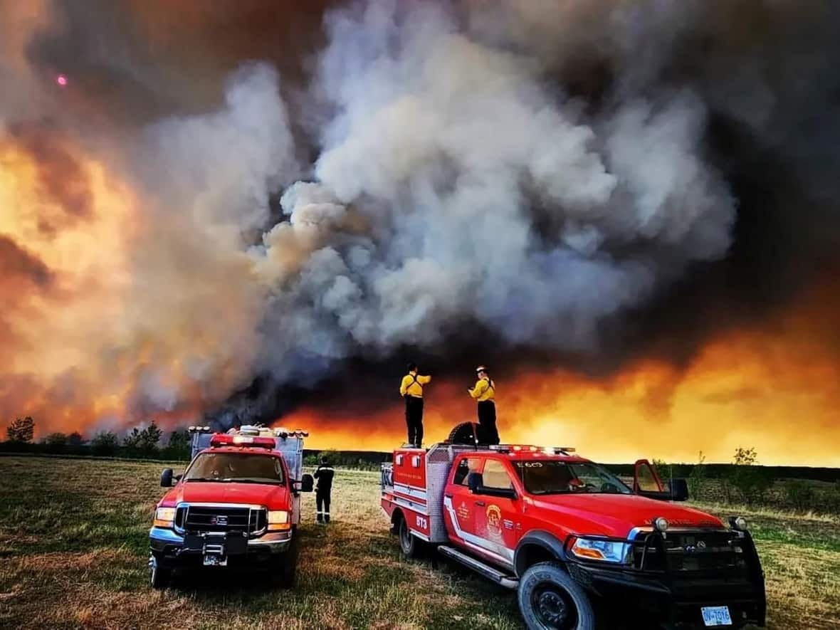 Firefighters stand on a Kamloops Fire Rescue truck at a wildfire near Fort St. John, B.C., earlier this week.  (Kamloops Fire Rescue/Handout via Reuters - image credit)