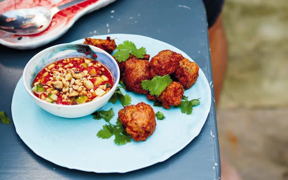 Blue plate with Thai fish cakes scattered with fresh coriander leaves and a bowl of sweet chilli dipping sauce topped with peanuts