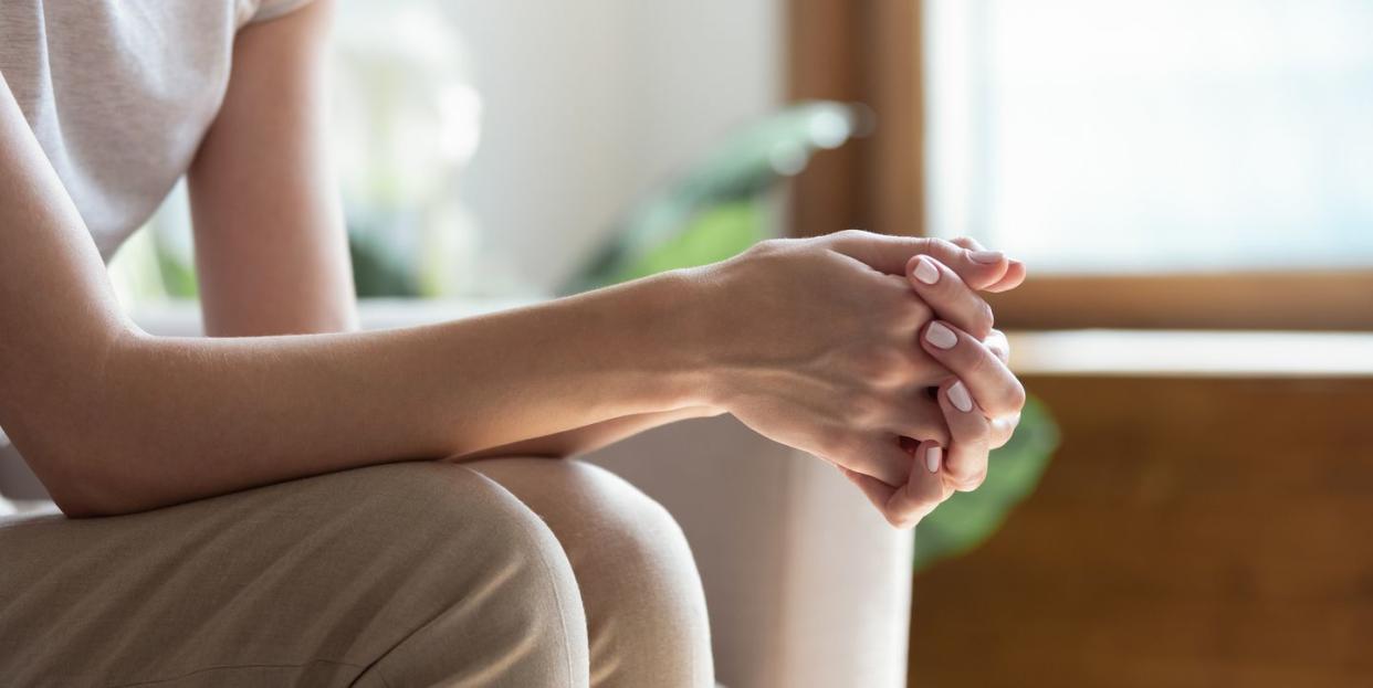 closeup woman sitting on sofa with folded hands on knees