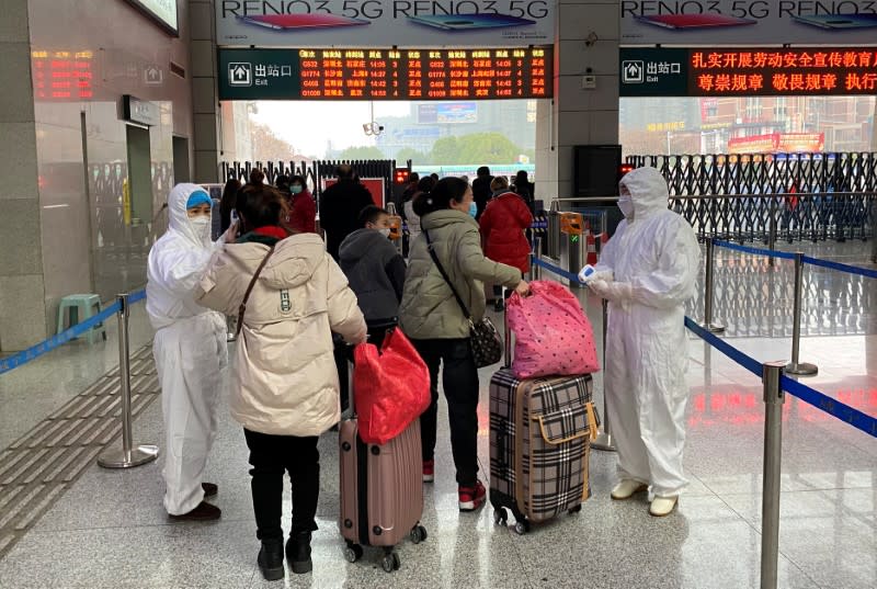 Workers in protective suits check temperatures of passengers arriving at the Xianning North Station on the eve of the Chinese Lunar New Year celebrations, in Xianning, a city bordering Wuhan