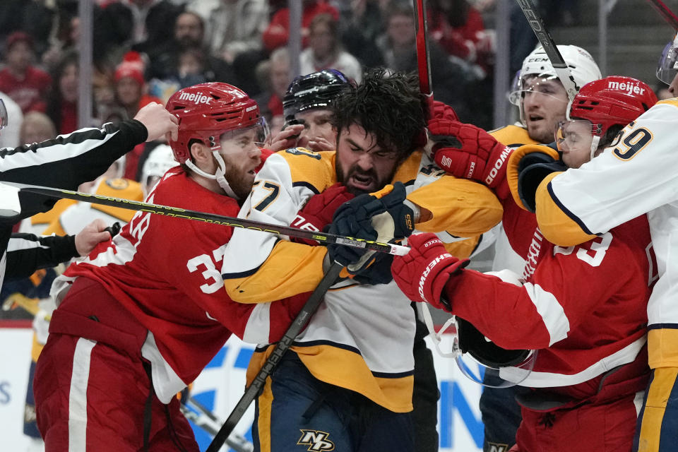 Nashville Predators defenseman Dante Fabbro (57) is pulled by Detroit Red Wings left wing J.T. Compher (37) and right wing Alex DeBrincat (93) during the second period of an NHL hockey game, Friday, Dec. 29, 2023, in Detroit. (AP Photo/Carlos Osorio)