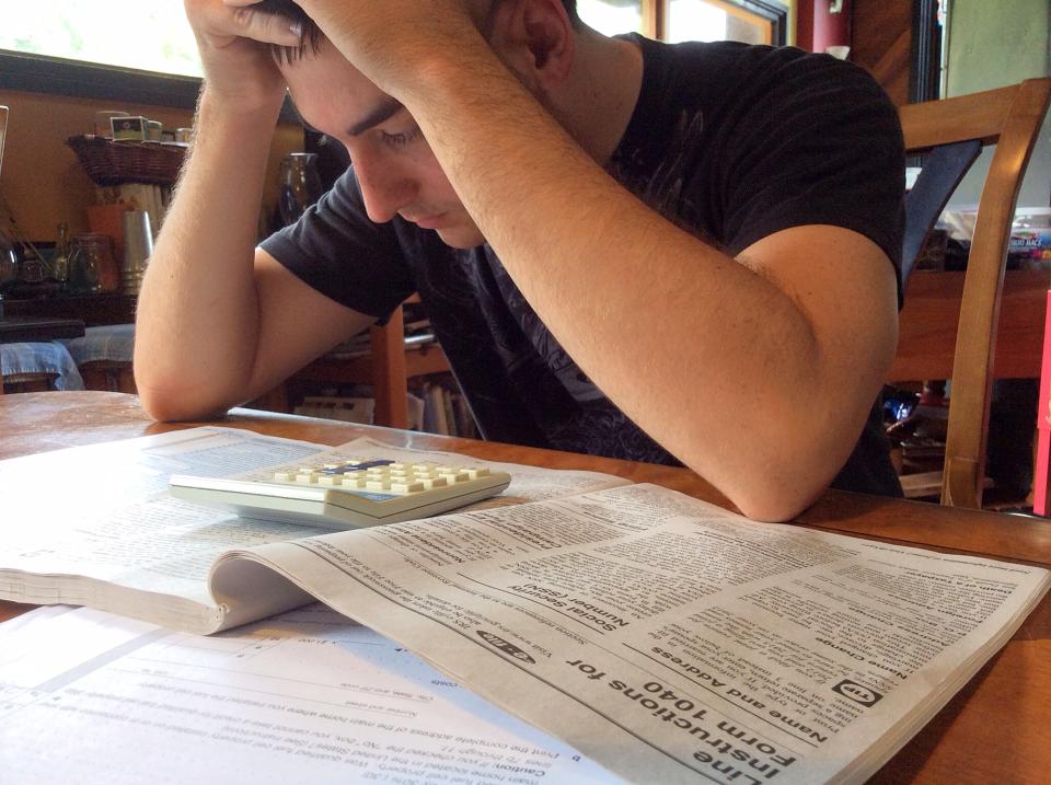 Man Looking Unhappy While Filling Out His U.S. 1040 Tax Form and looking at Tax Instruction Book