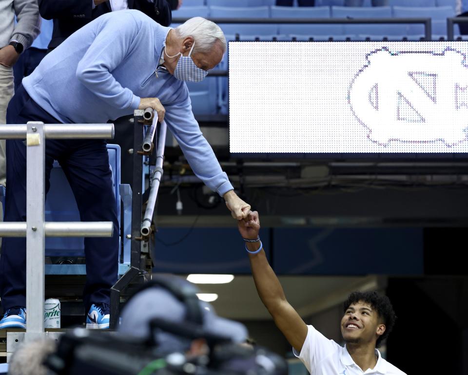 Former head coach Roy Williams of the North Carolina Tar Heels fist-bumps Puff Johnson #14 before their game against the Loyola Greyhounds at the Dean E. Smith Center on November 09, 2021 in Chapel Hill, North Carolina.