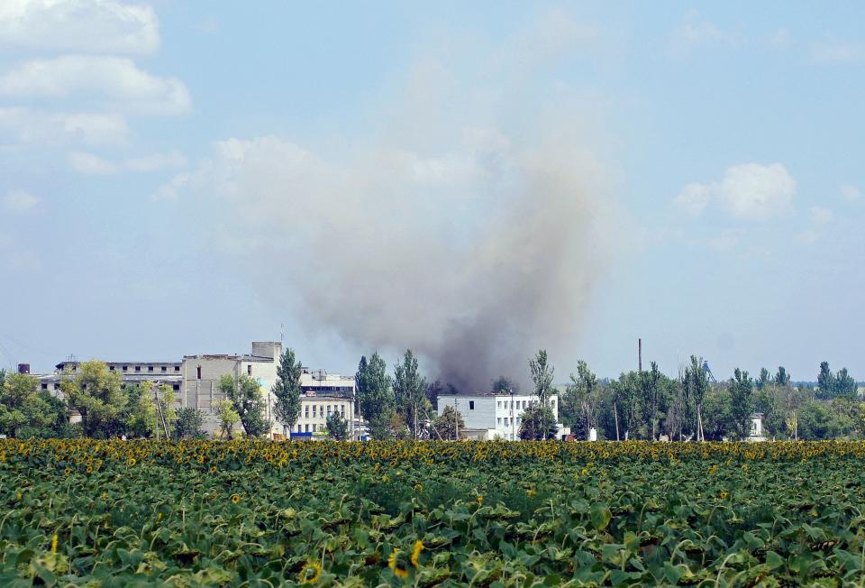 smoke rising over buildings in the distance of a green field