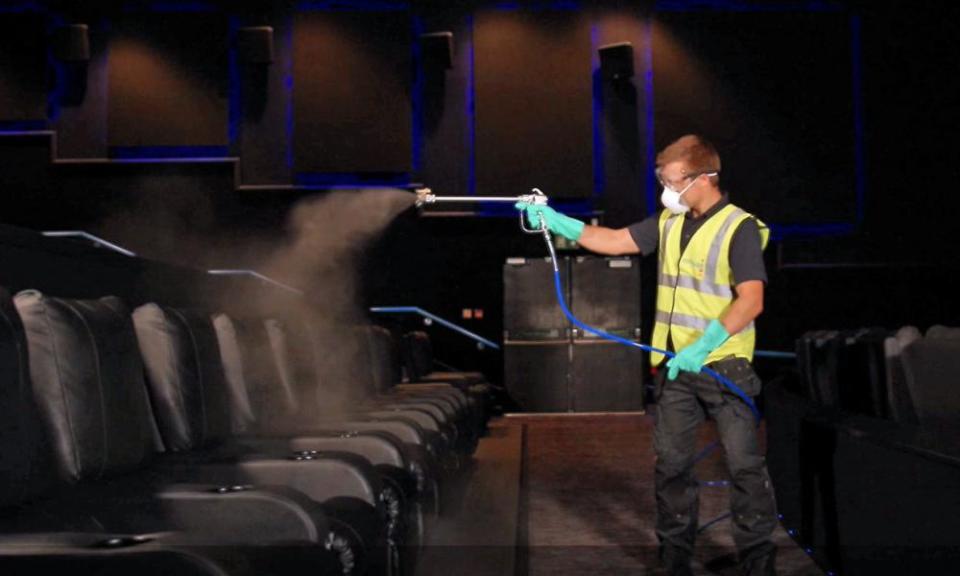 A man in a hi-vis tabard spraying cinema seats with cleanser