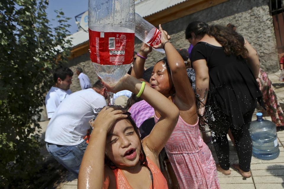 Dos niñas juegan a refrescarse mientras residentes juntan agua en una comuna de Santiago, Chile, el lunes 27 de febrero de 2017. Millones de personas se quedaron sin agua potable en la zona metropolitana de la capital chilena tras inundaciones y deslaves, que provocaron escasez. (AP Foto/Esteban Félix)