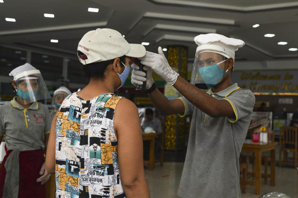 A woman is checked body temperature to help curb the spread of the new coronavirus at the entrance of a tea-shop in Yangon, Myanmar Monday, May 18, 2020. (AP Photo/Thein Zaw)