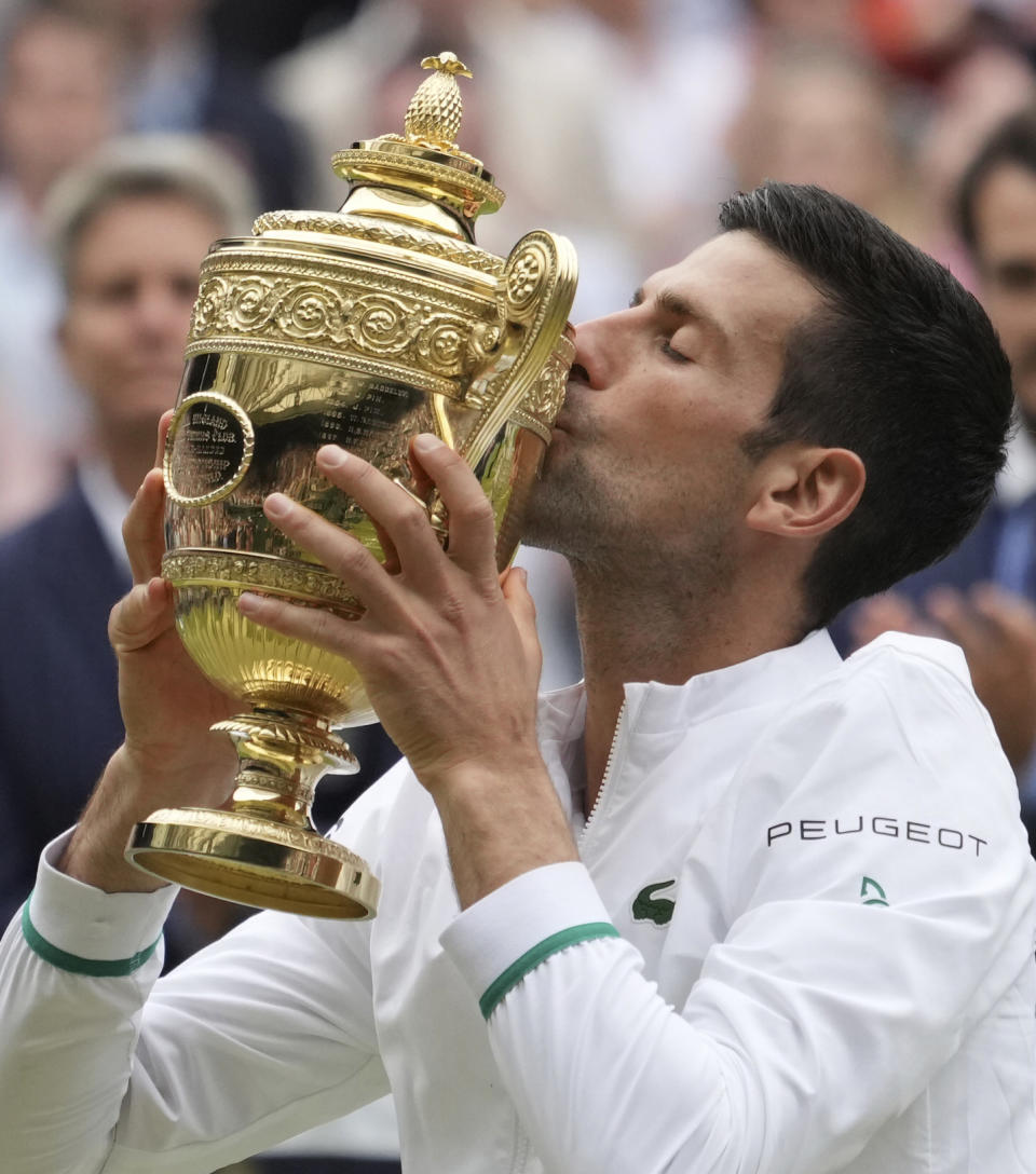 Serbia's Novak Djokovic kisses his winner's trophy and celebrates his victory over Italy's Matteo Berrettini during the men's singles final match on day thirteen of the Wimbledon Tennis Championships in London, Sunday, July 11, 2021. (AP Photo/Alberto Pezzali)