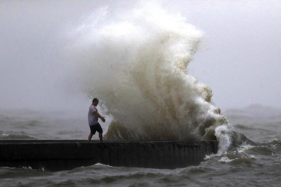 A wave crashes as a man stands on a jetty near Orleans Harbor in Lake Pontchartrain in New Orleans, Sunday, June 7, 2020, as Tropical Storm Cristobal approaches the Louisiana Coast. (AP Photo/Gerald Herbert)