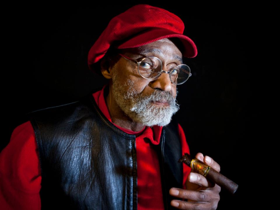 Melvin Van Peebles in a red cap and holding a cigar