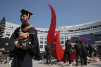 A graduate student stands as protesters paste posters on a sculpture after disrupting a graduation ceremony to set up a makeshift memorial at the University of Science and Technology in Hong Kong on Friday, Nov. 8, 2019. The ceremony was cut short, and black-clad masked students turned the stage into a memorial for Chow Tsz-Lok who fell off a parking garage after police fired tear gas during clashes with anti-government protesters and died Friday. (AP Photo/Kin Cheung)