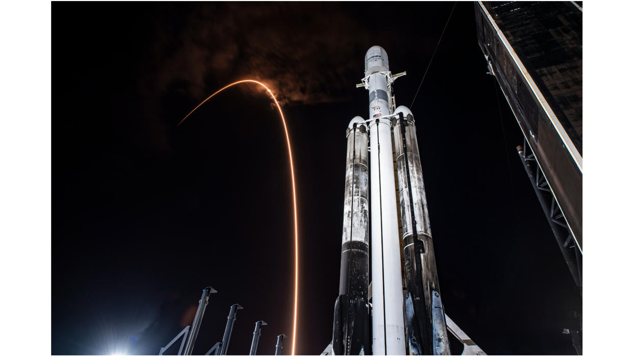  a falcon 9 rocket carves an orange arc in the sky behind a black-and-white falcon heavy rocket 