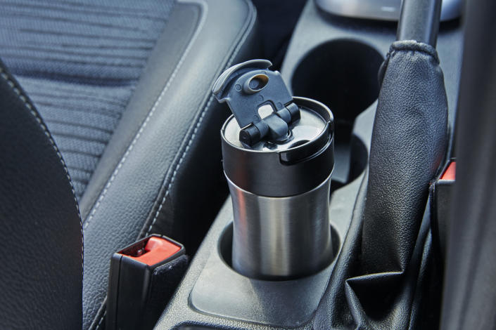 Close-up of a reusable metal coffee cup or cup holder in a car with a gear stick and handbrake