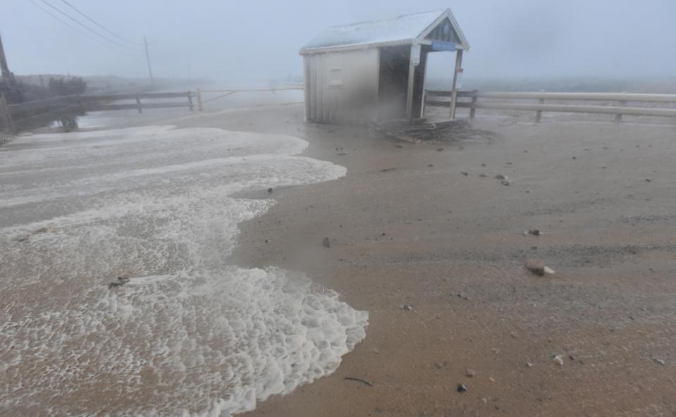 High tide water from Cape Cod Bay washes over the protective dune and floods the parking lot at Town Neck Beach in Sandwich at high tide on Saturday morning.