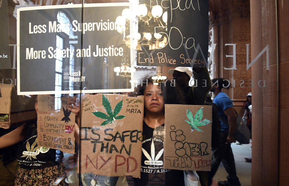 Pilar DeJesus with a coalition of protesters urging legislators to pass Marijuana legislation holds a sign against the senate lobby doors at the state Capitol Wednesday, June 19, 2019, in Albany, N.Y. (AP Photo/Hans Pennink)
