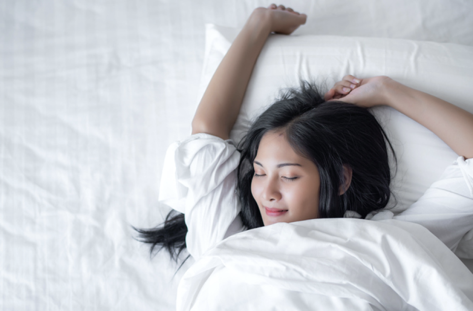 Woman lying in bed stretching with her eyes closed