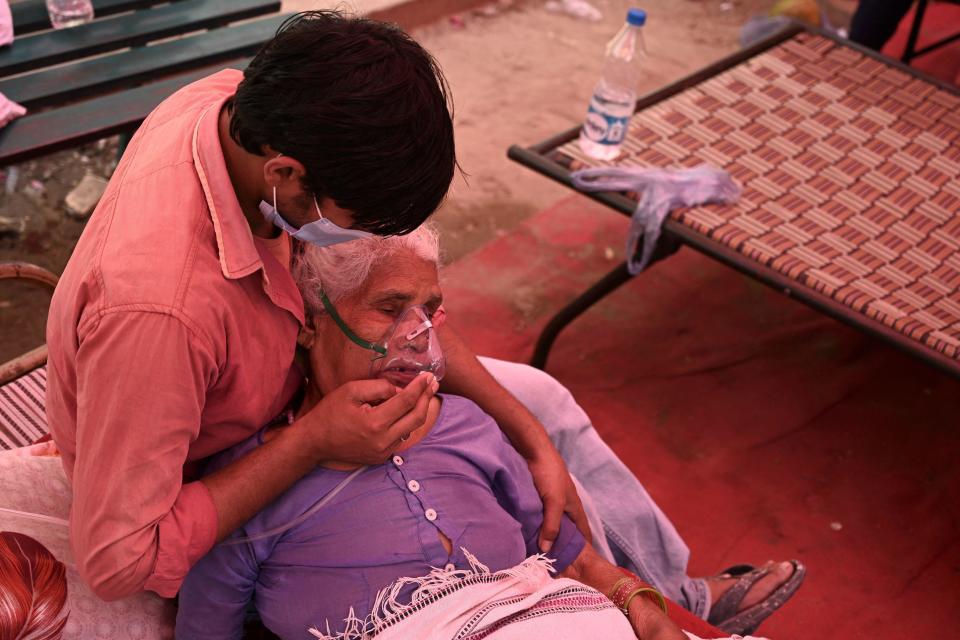 A family member comforts a woman breathing with the help of oxygen being provided by a Gurdwara, a place of worship for Sikhs, under a tent installed along the roadside as the COVID-19 pandemic hits Ghaziabad, India, on May 4, 2021. / Credit: TAUSEEF MUSTAFA/AFP/Getty