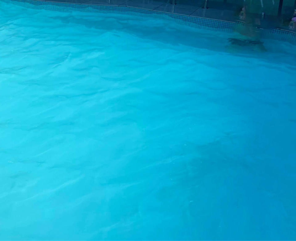 A child at the bottom of a backyard swimming pool is barely visible at the surface.